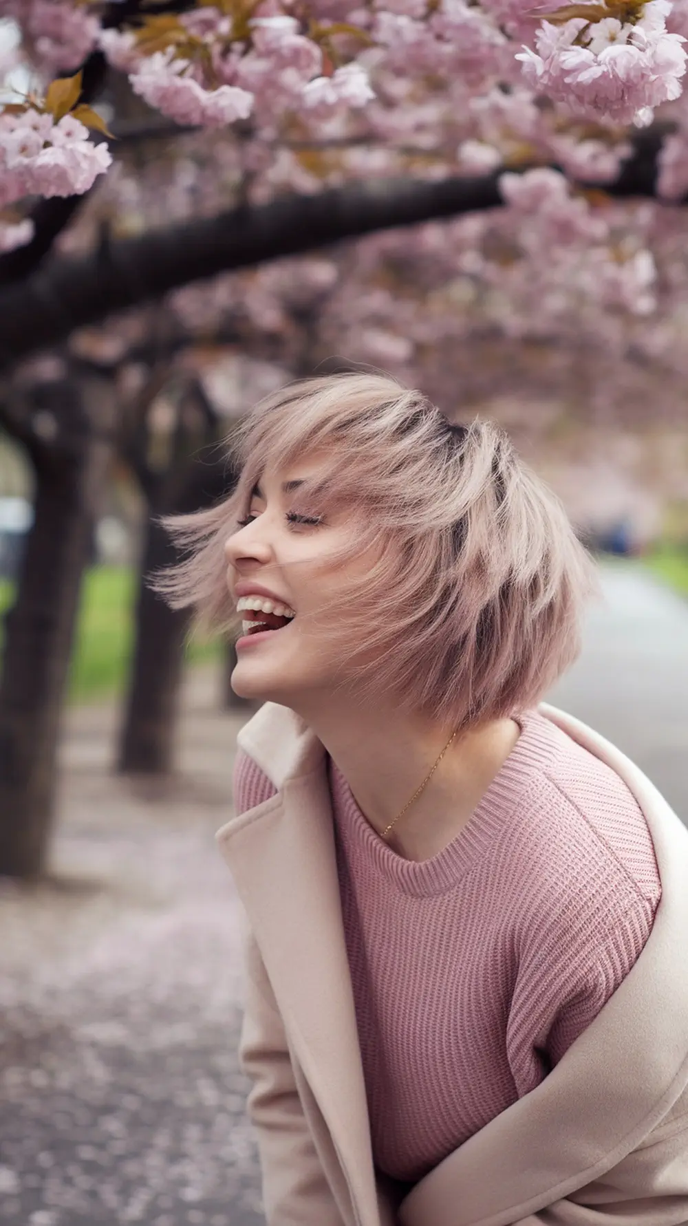 A woman with a playful layered haircut smiling under cherry blossom trees