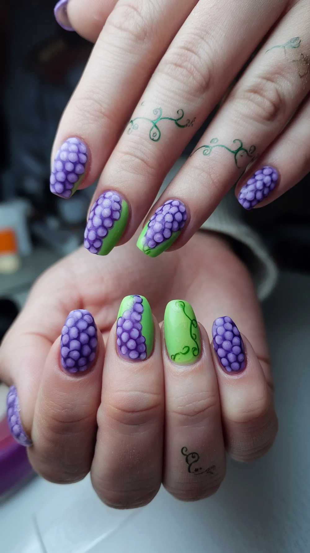 Nails painted with grape designs on a green background