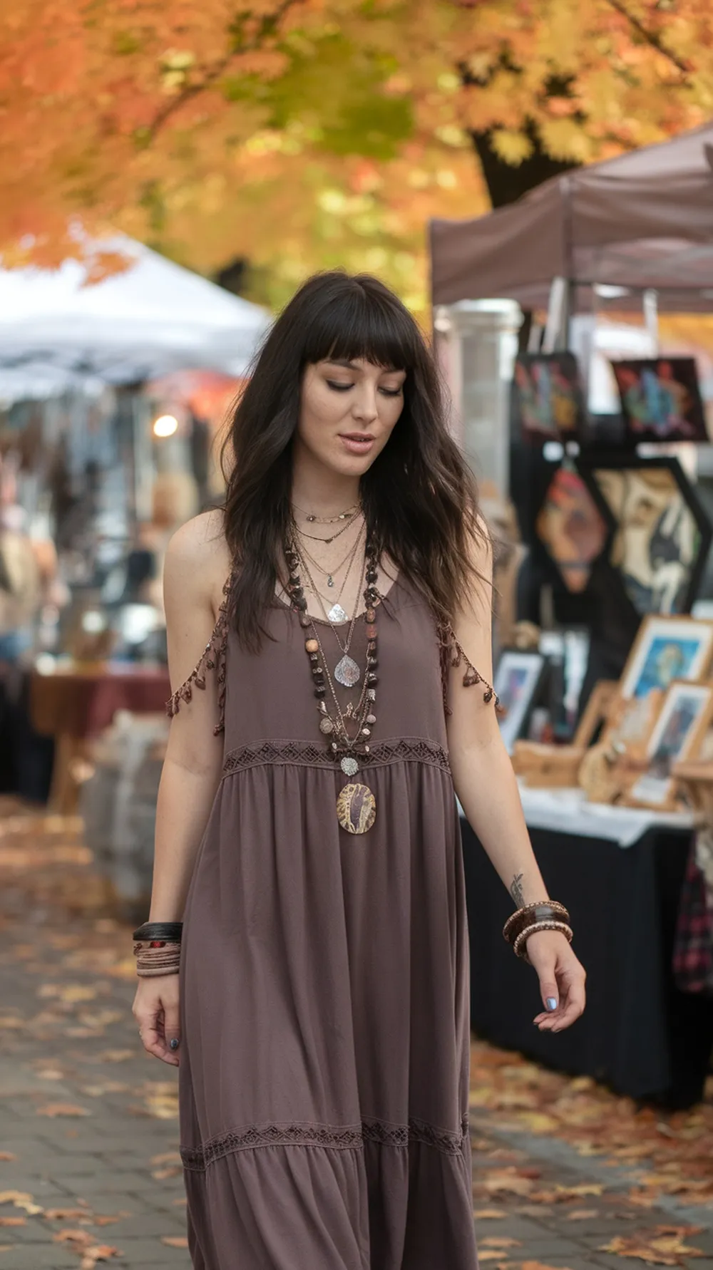 A woman in a brown bohemian maxi dress with layered jewelry walking through an autumn market.